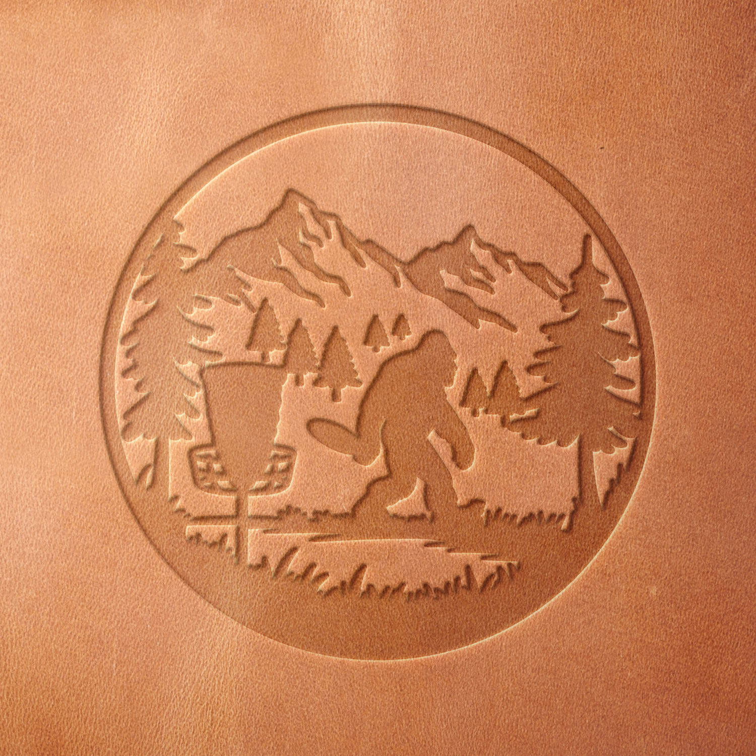 Leather sample showcasing a Bigfoot playing disc golf design, stamped with a Delrin leather stamp, featuring a mountainous forest scene with trees and a disc golf basket.