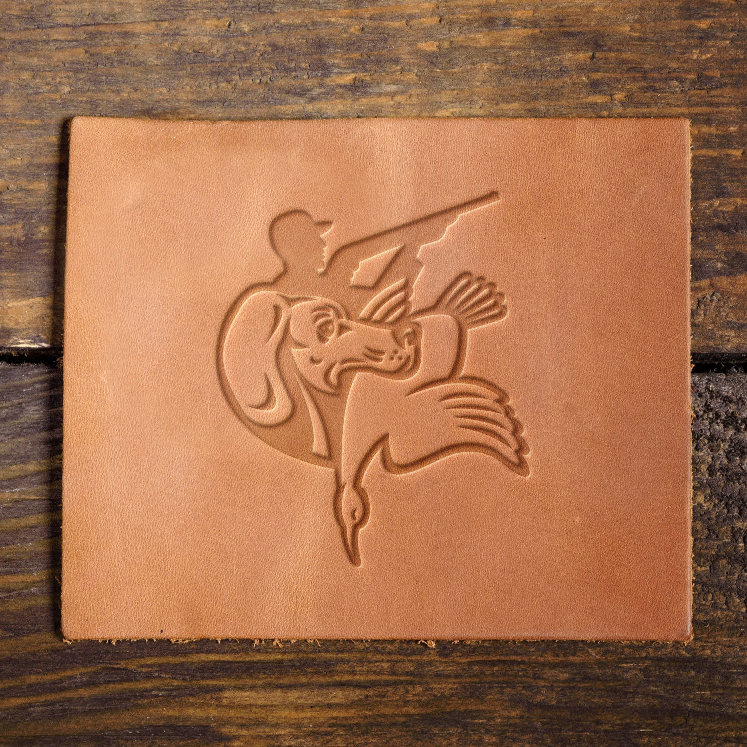 Leather sample featuring a stamped hunting scene using a Delrin leather stamp, showcasing a retriever with a duck and a hunter in silhouette, ideal for outdoor and hunting-themed leathercraft.