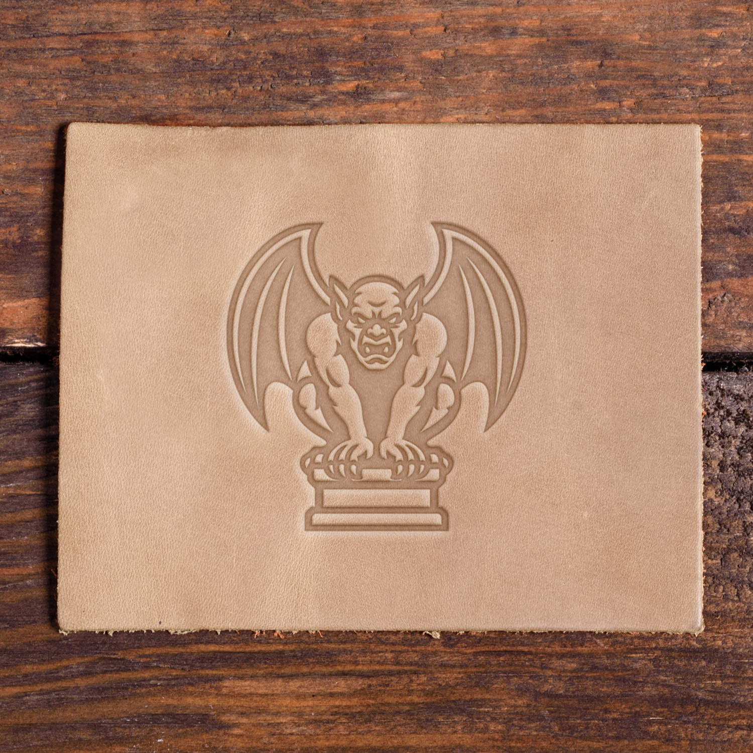 Leather piece stamped with a Delrin leather stamp design of a gargoyle perched on a pedestal with wide wings and a fierce face.