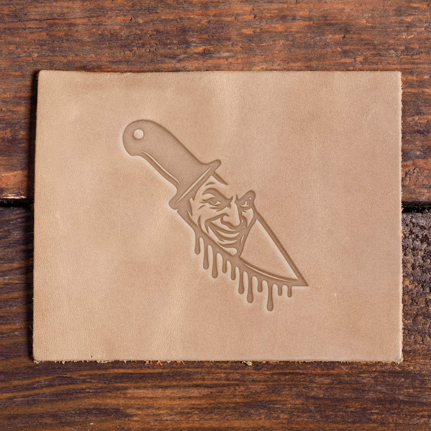 Leather piece stamped with a Delrin leather stamp design of a knife featuring a creepy smiling face on the blade and dripping detail below, perfect for Halloween-themed projects.