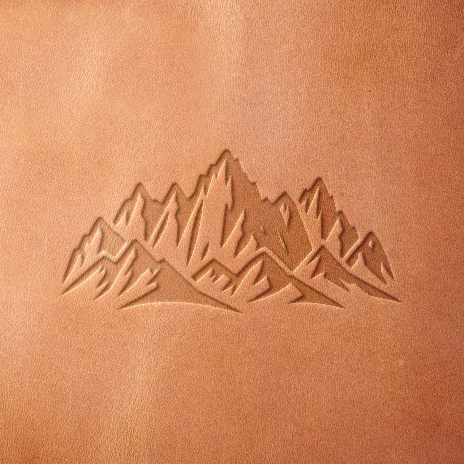 Leather sample showcasing a mountain range design, stamped with a Delrin leather stamp, highlighting the jagged peaks and natural contours of the landscape.