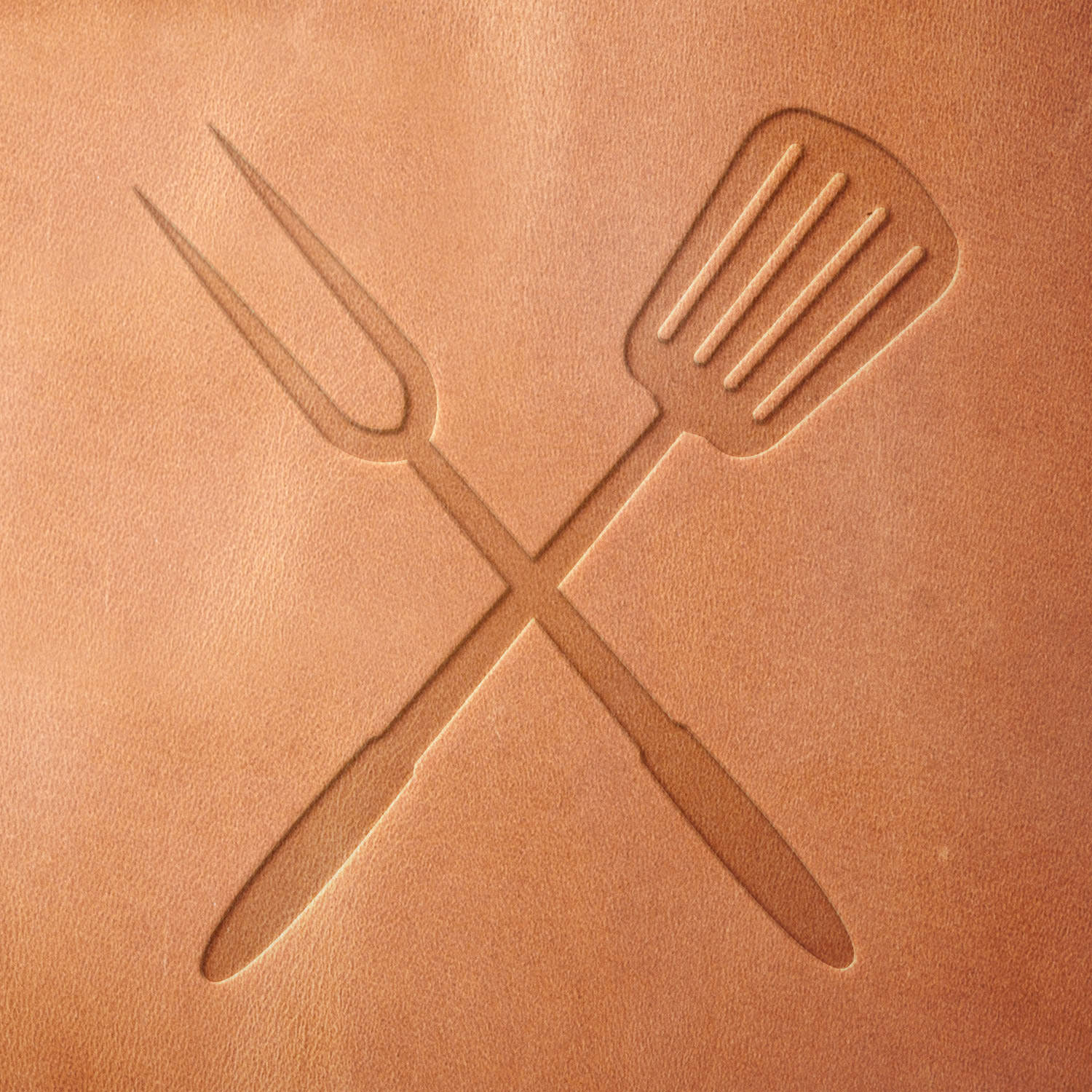 Leather sample showcasing a stamped grilling tools design using a delrin leather stamp, emphasizing the utensils’ sleek shape and balanced crossed layout.