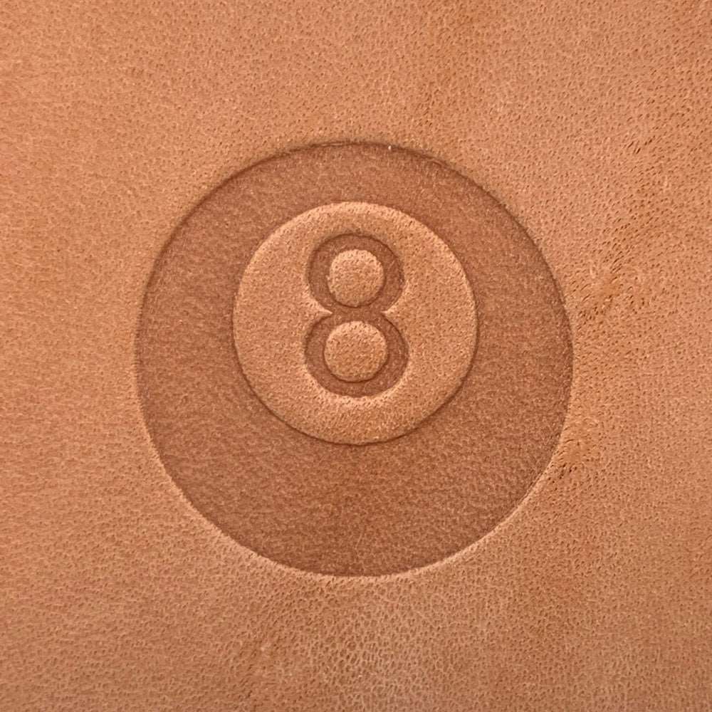 Veg-tan leather stamped with an eight ball billiards design using a Delrin leather stamp, showing a clean, centered impression.