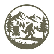 Bigfoot playing disc golf in a forested mountain landscape, framed within a circular border. The design captures a mythical creature in an unexpected outdoor activity.