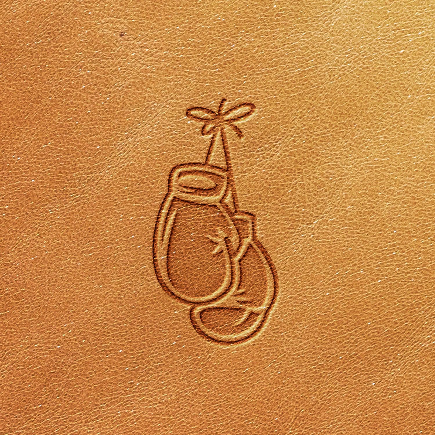 The Boxing Glove Delrin Leather Stamp showcases a design of boxing gloves hanging by their laces, depicted in a simple, minimalist style. The natural tan color and textured appearance of the leather add character to this unique piece.