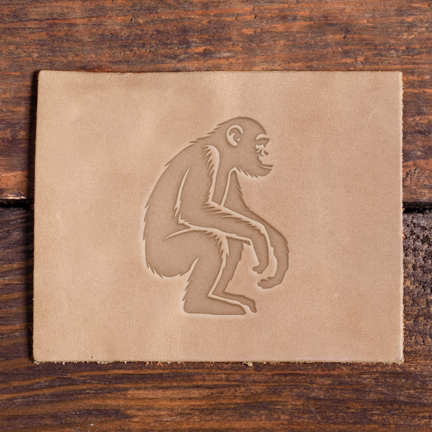 Leather piece stamped with a Delrin leather stamp design of a seated chimpanzee with long limbs and textured fur detailing.