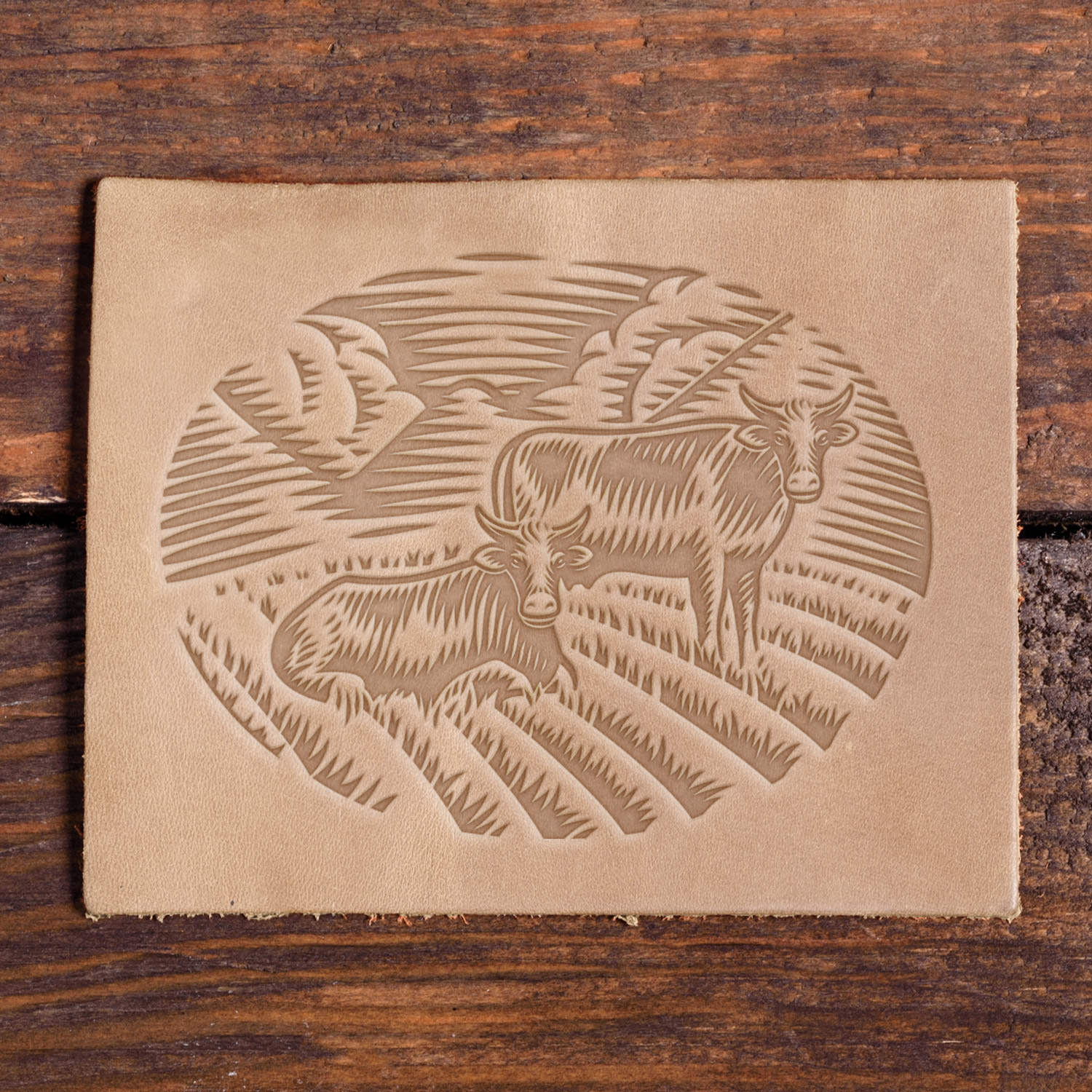 Two cows in a field with clouds and crops, stamped with a Delrin leather stamp