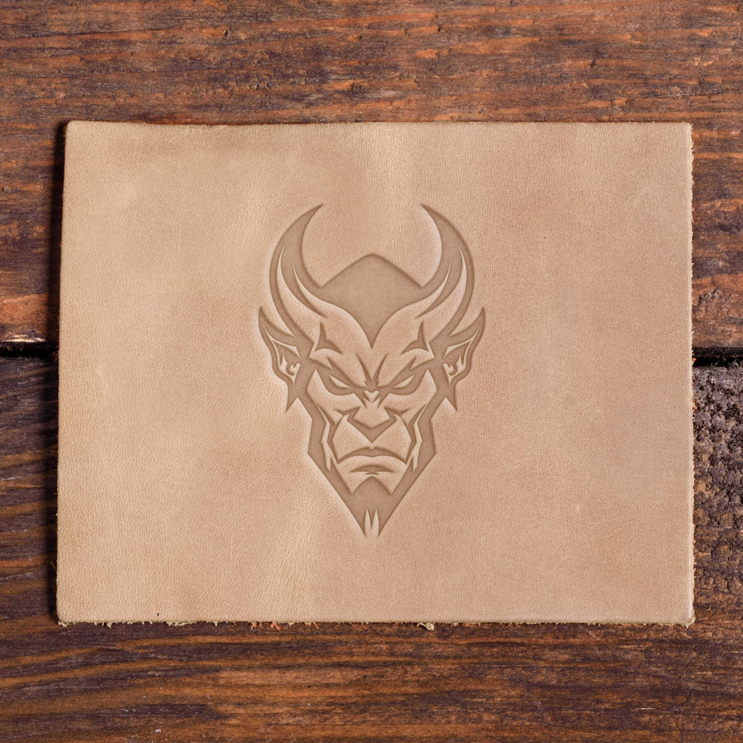 Leather piece stamped with a Delrin leather stamp design of a horned devil face featuring bold lines and a fierce look.