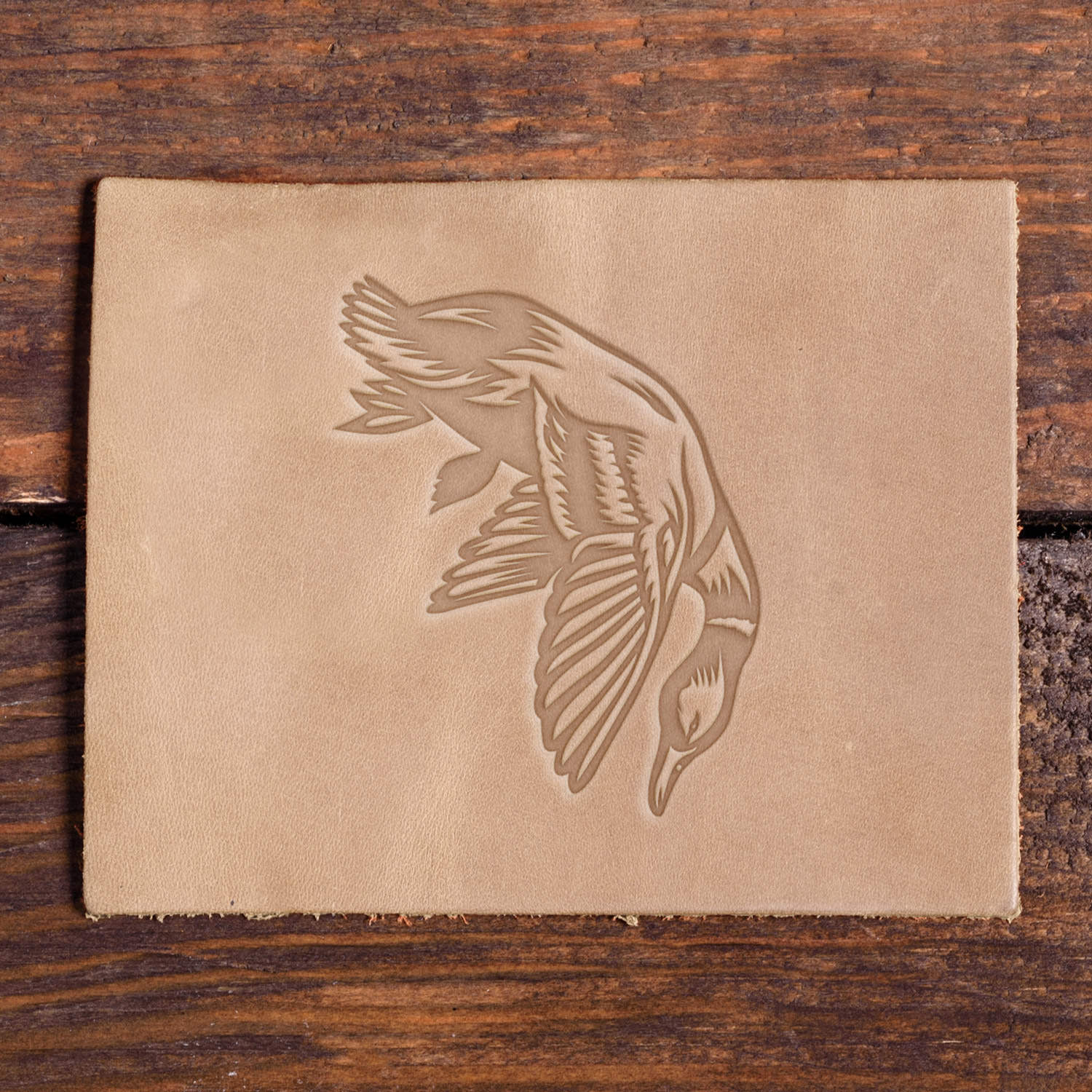 Leather piece stamped with a Delrin leather stamp design of a duck dropping midair after being shot, ideal for bird hunting and outdoor sportsman leatherwork.