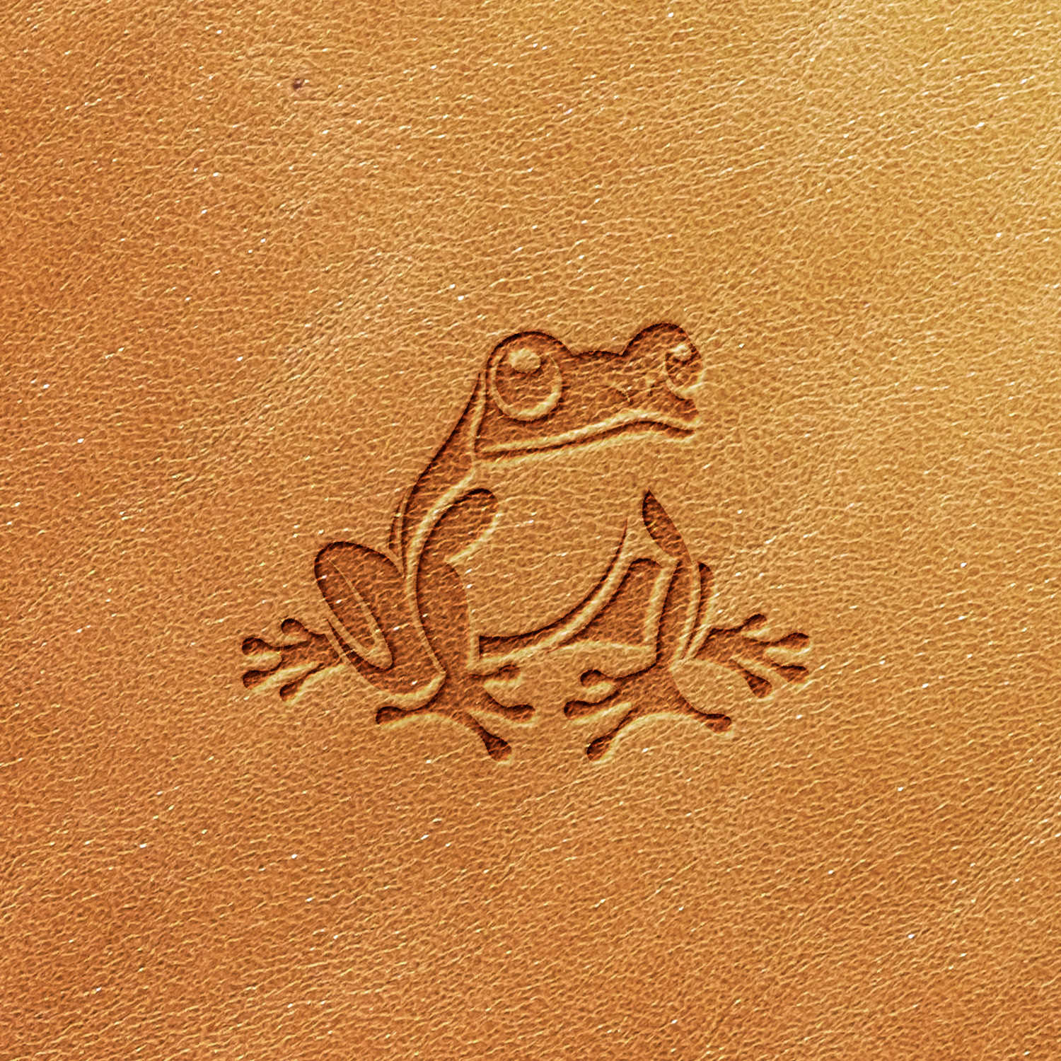 The Frog Delrin Leather Stamp features an intricate image of a frog set against a smooth, tan leather background. The frog's legs, eyes, and simple body design are clearly defined, with the detailed texture of the leather enhancing the overall aesthetic.