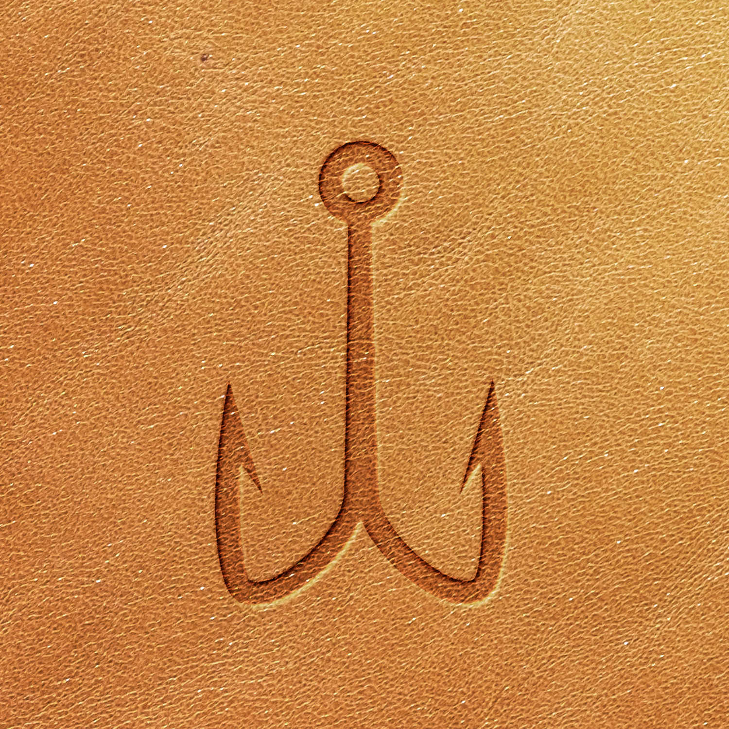 The Fish Hook Delrin Leather Stamp features a double hook design with two sharp points and a circular eye loop at the top, intricately embossed on a smooth, tan leather surface. This combination gives the leather an elegant and refined look.