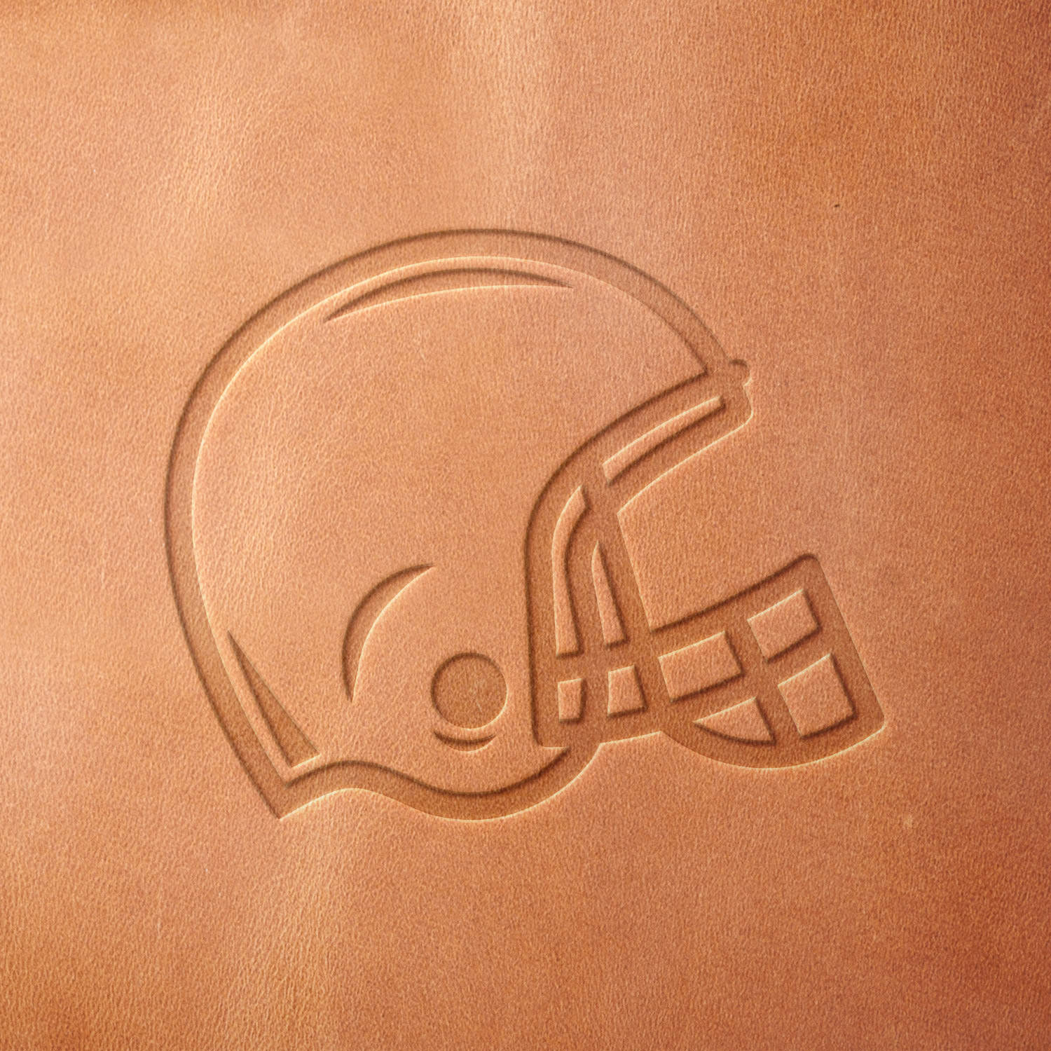 Leather sample showcasing a stamped football helmet design using a delrin leather stamp, highlighting the helmet’s protective shape and bold outline.