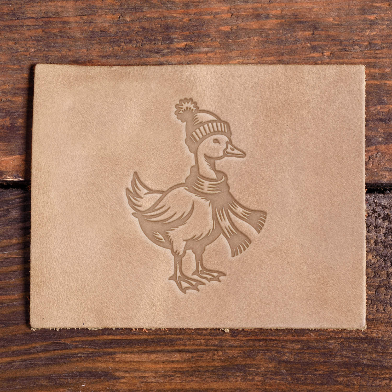 Leather piece stamped with a Delrin leather stamp design of a duck dressed in a knit hat and scarf, perfect for winter leather projects.