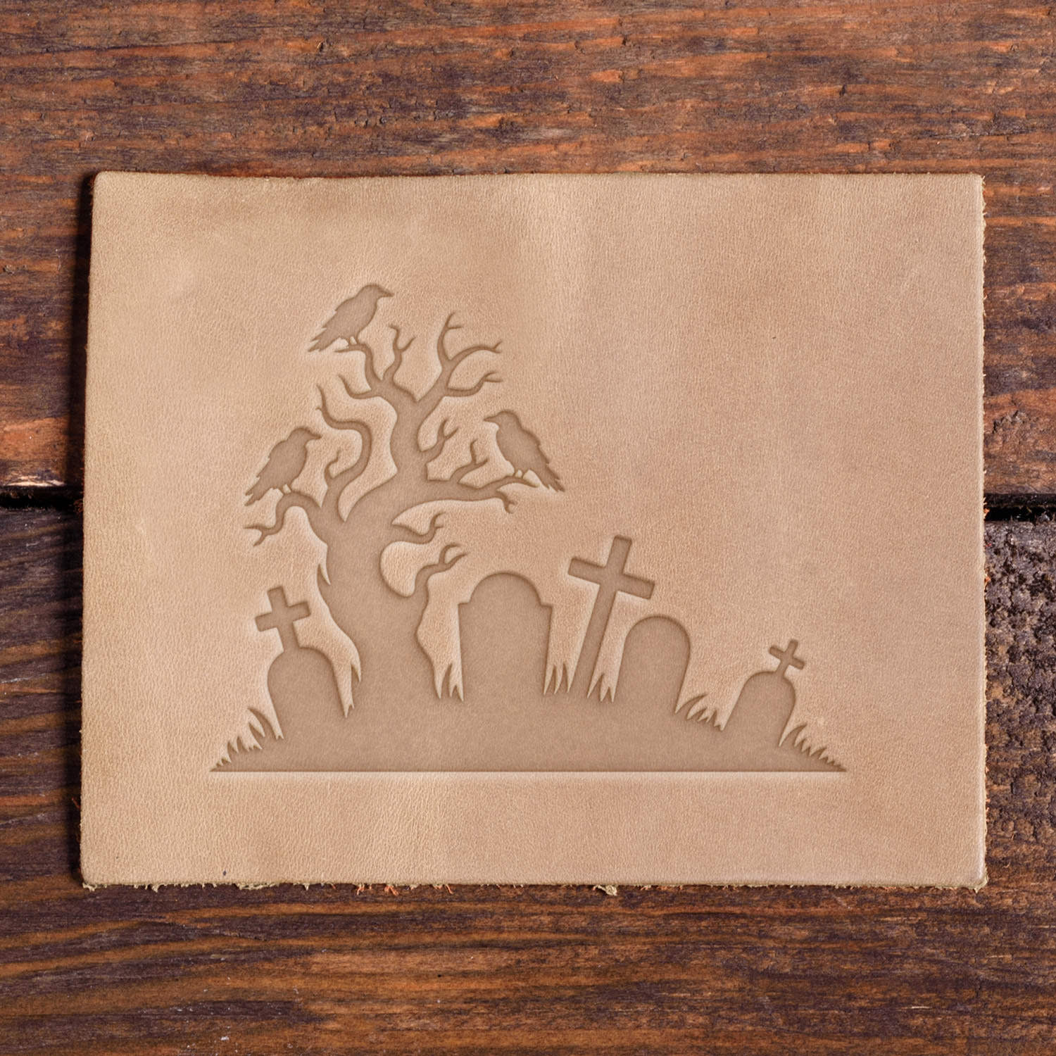 Leather piece stamped with a Delrin leather stamp design of a haunted cemetery featuring crooked tombstones, eerie tree branches, and crows.