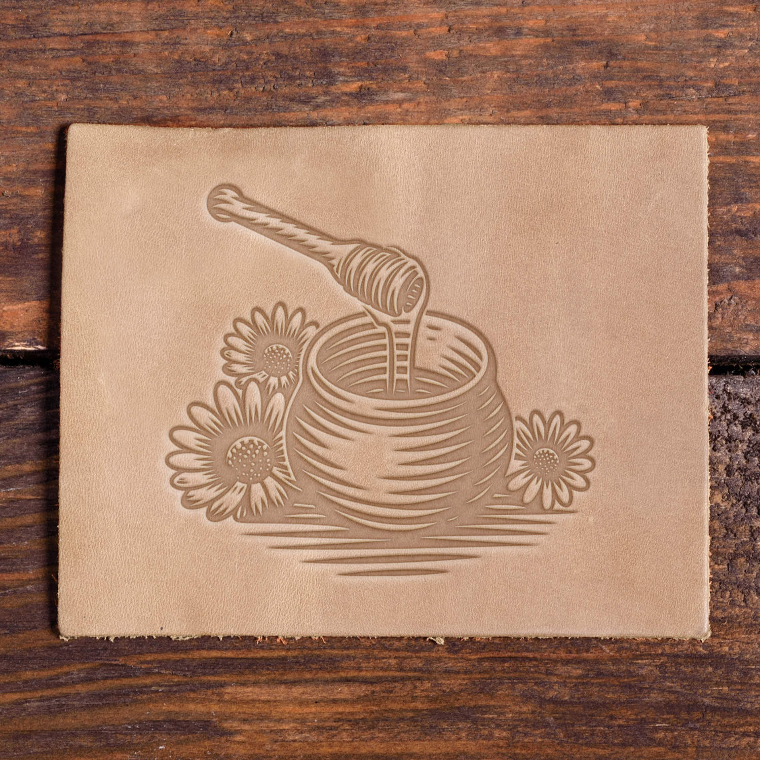 Stamped leather impression of a honey jar with dipper and daisies made using a Delrin leather stamp