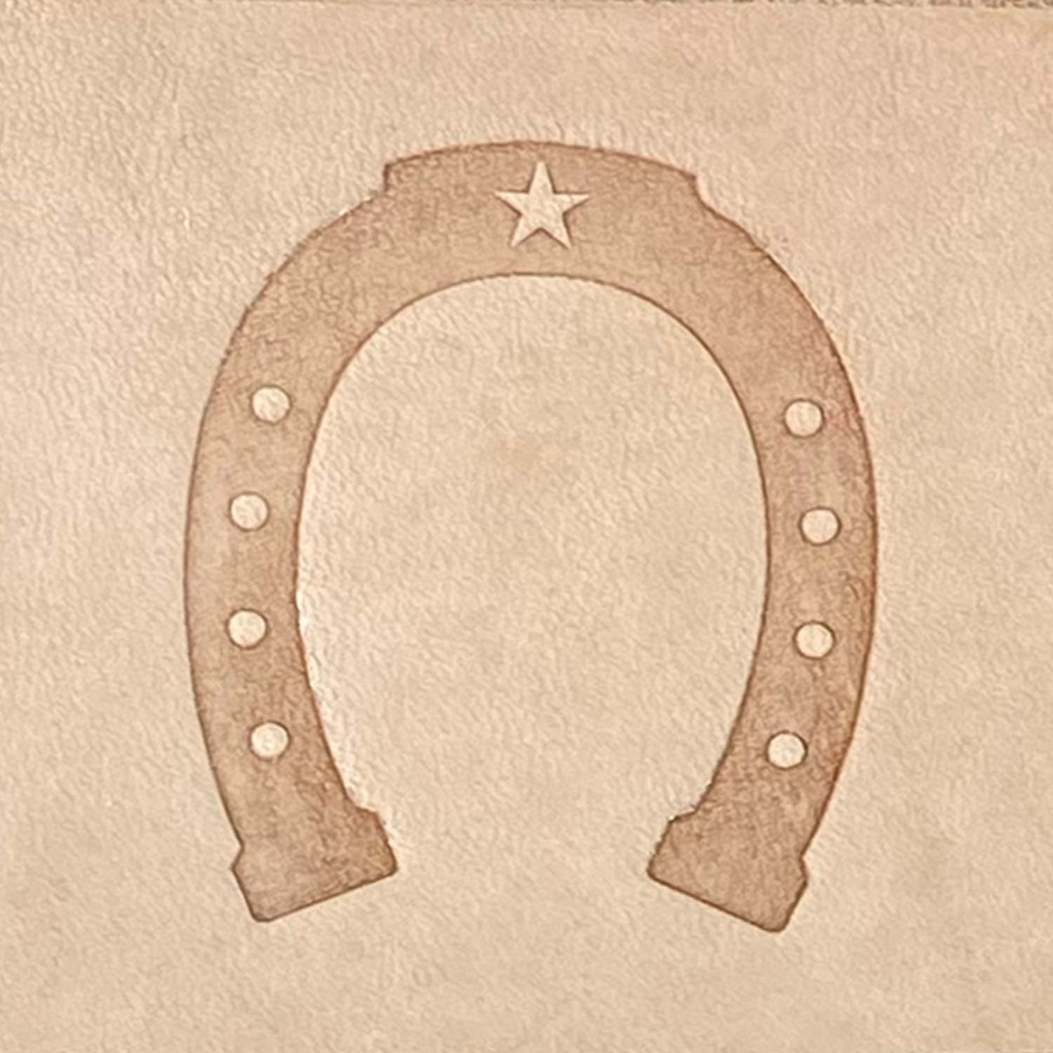 Leather sample stamped with a Delrin leather stamp, showcasing a horseshoe with a star detail and traditional nail hole accents.