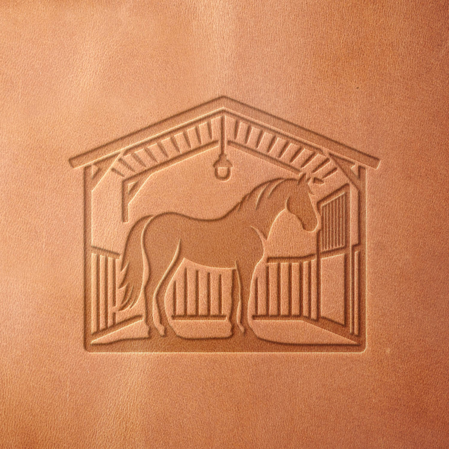 Leather sample stamped with a Delrin leather stamp, showcasing a horse inside a barn with wooden beams, fencing, and a hanging lantern.