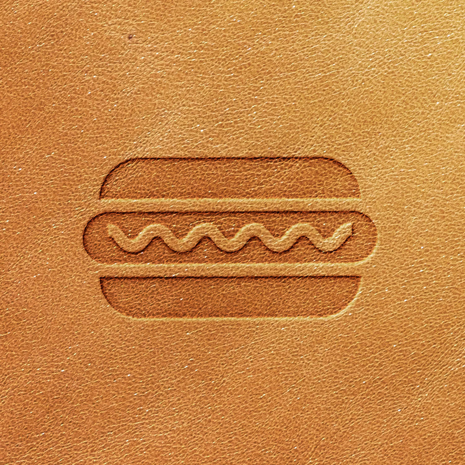 The Hot Dog Delrin Leather Stamp features a stylized embossing of a hot dog with wavy lines representing mustard or ketchup on a light brown leather surface.