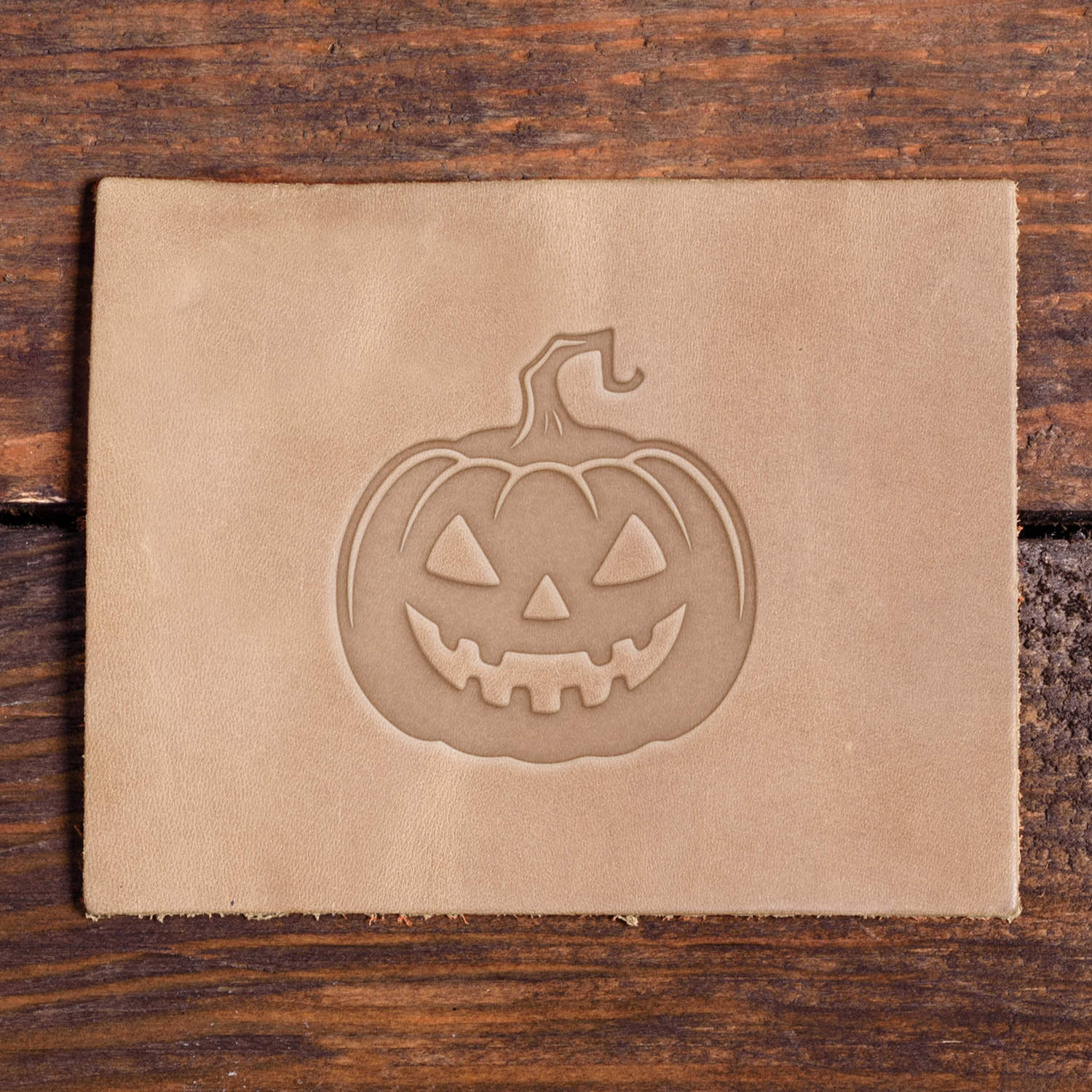 Leather piece stamped with a Delrin leather stamp design of a spooky jack-o’-lantern face with fanged teeth and a twisted stem.