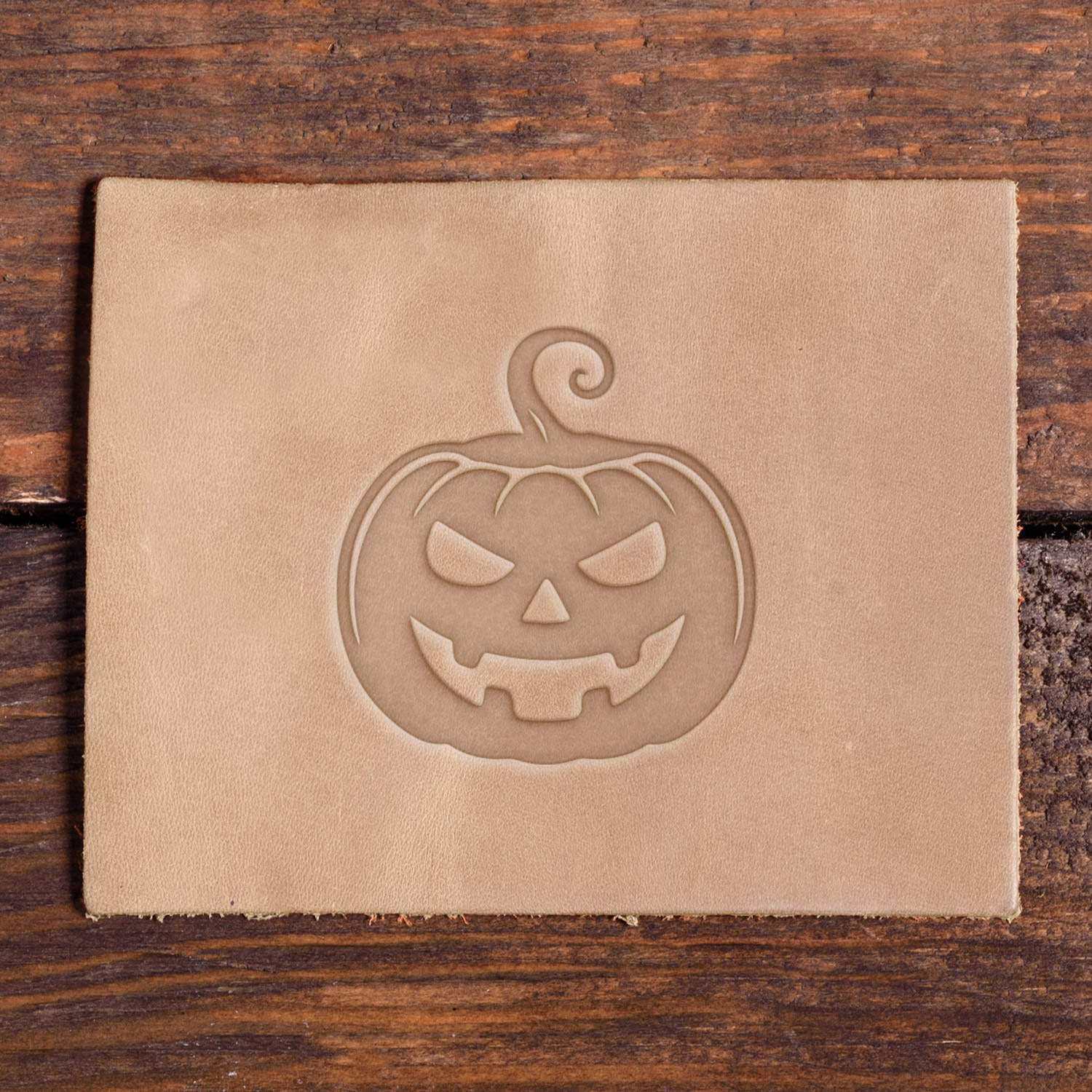 Leather piece stamped with a Delrin leather stamp design of a spooky jack-o’-lantern face with fanged teeth and a twisted stem.