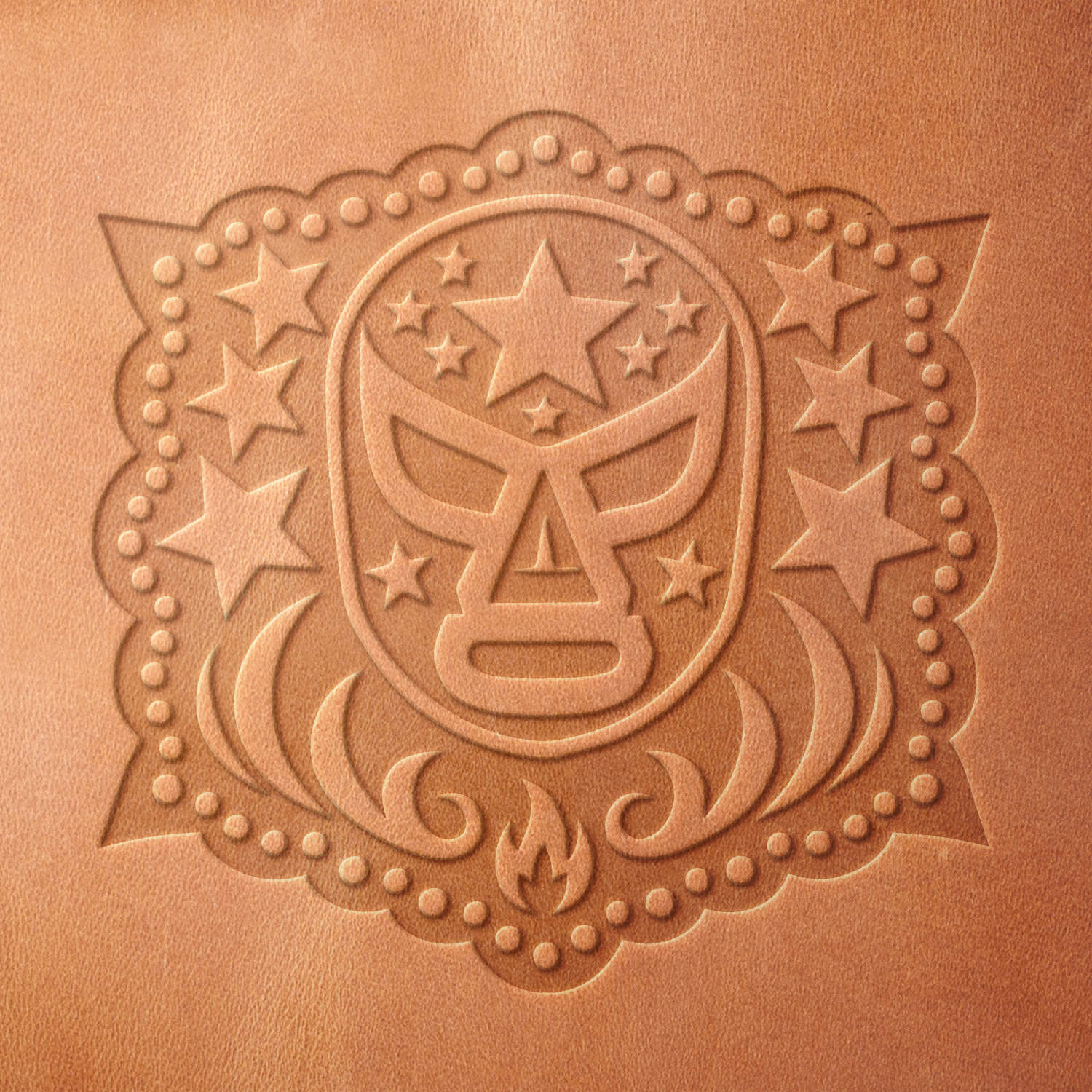 Leather sample showcasing a stamped lucha libre mask design using a delrin leather stamp, highlighting the bold mask outline, star details, and intricate border.
