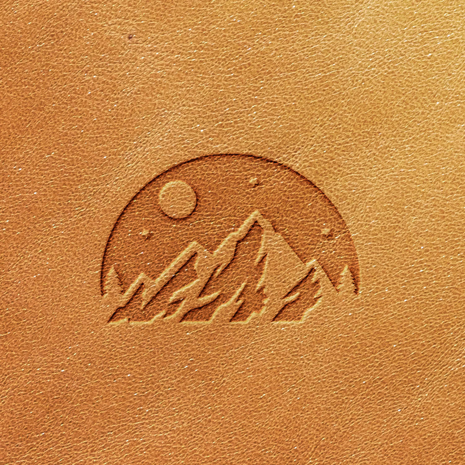 The Mountain Night Sky Scene Delrin Leather Stamp features a leather surface embossed with an illustration of a mountain range beneath a crescent moon and stars, all enclosed within a semi-circle. The intricate design stands out with its darker tone compared to the surrounding leather.