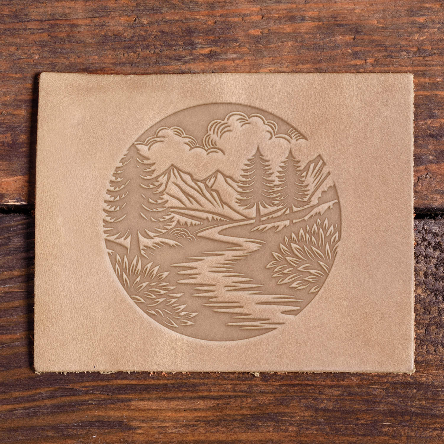 Mountain and river scene with pine trees and shrubs stamped into leather using a Delrin leather stamp