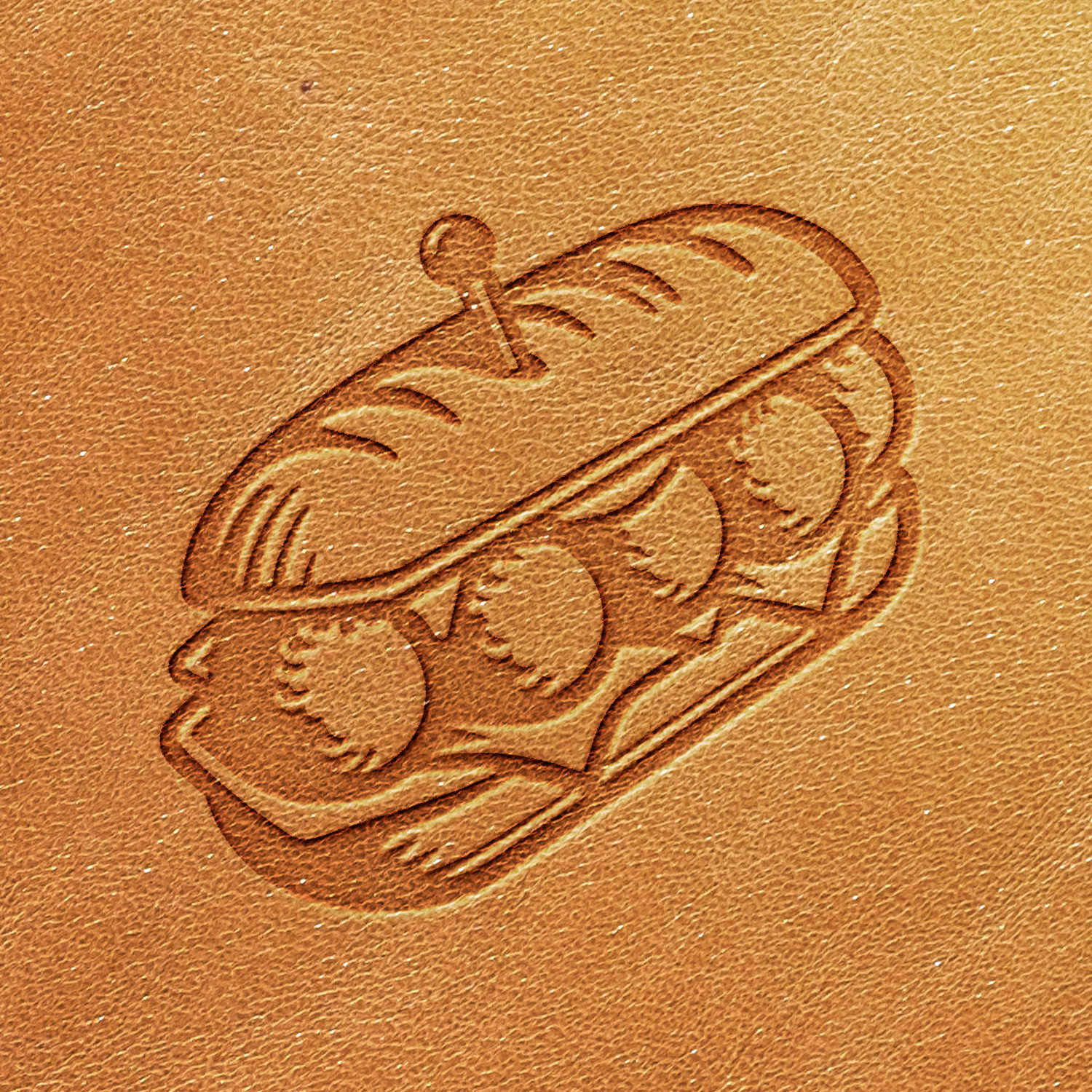 The Meatball Sandwich Delrin Leather Stamp features a detailed engraving of a submarine sandwich, with layers of meatballs, cheese, and vegetables held together by a toothpick. The image is set against a brown, textured background resembling leather.