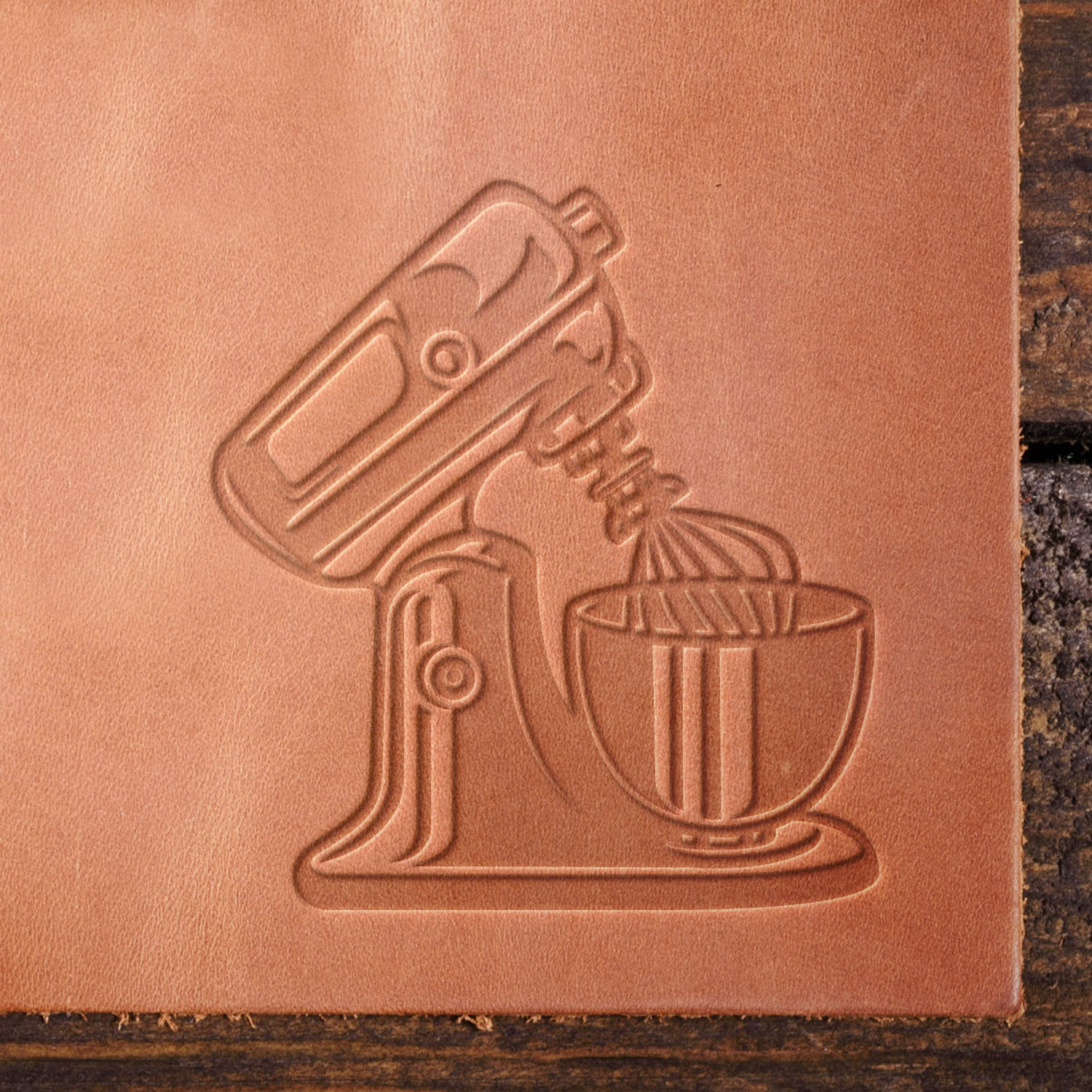 Leather sample showcasing a stamped stand mixer design using a delrin leather stamp, highlighting the detailed contours of the mixer, whisk, and bowl.