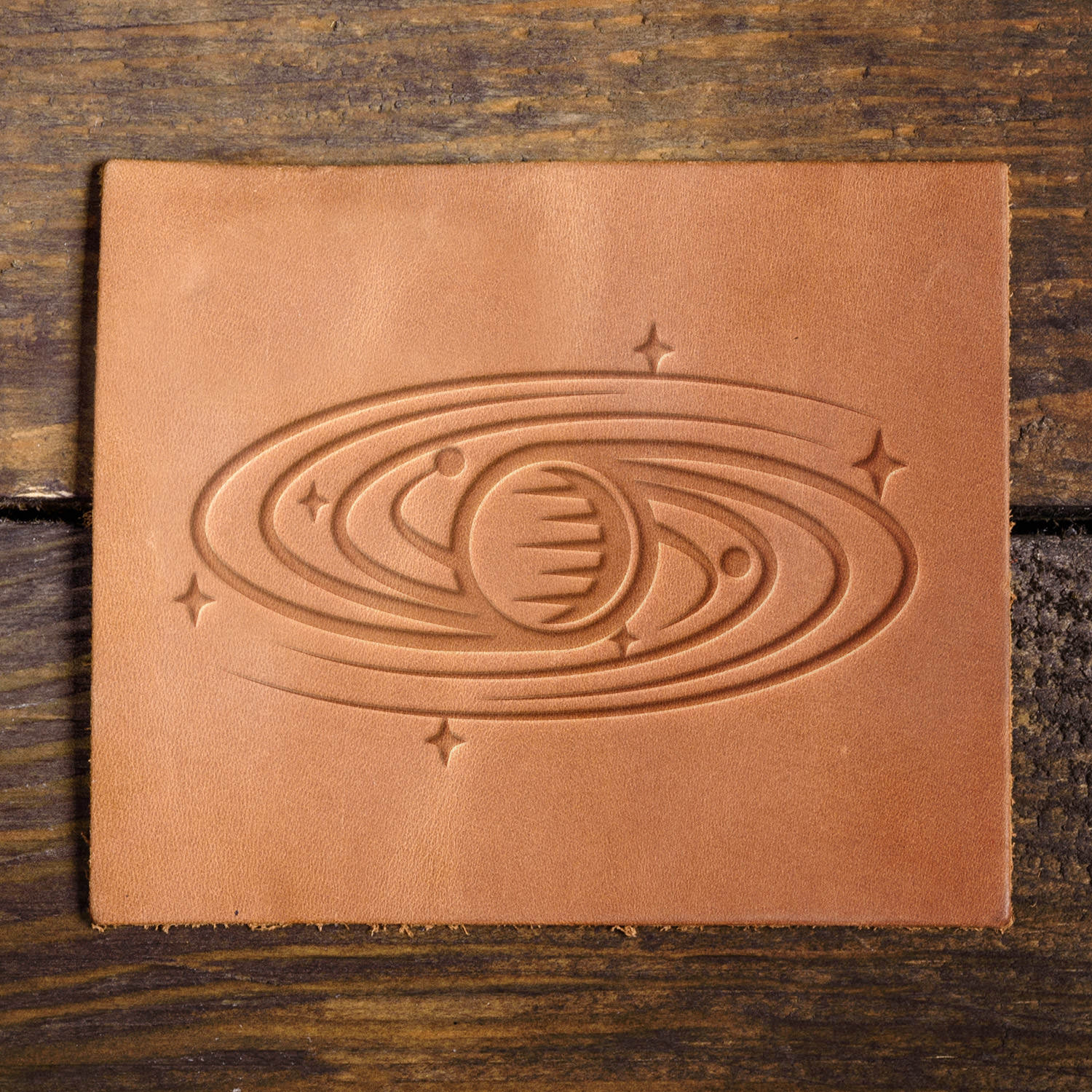 Leather sample featuring a stamped planet with swirling rings and stars, perfect for space-themed leather projects.