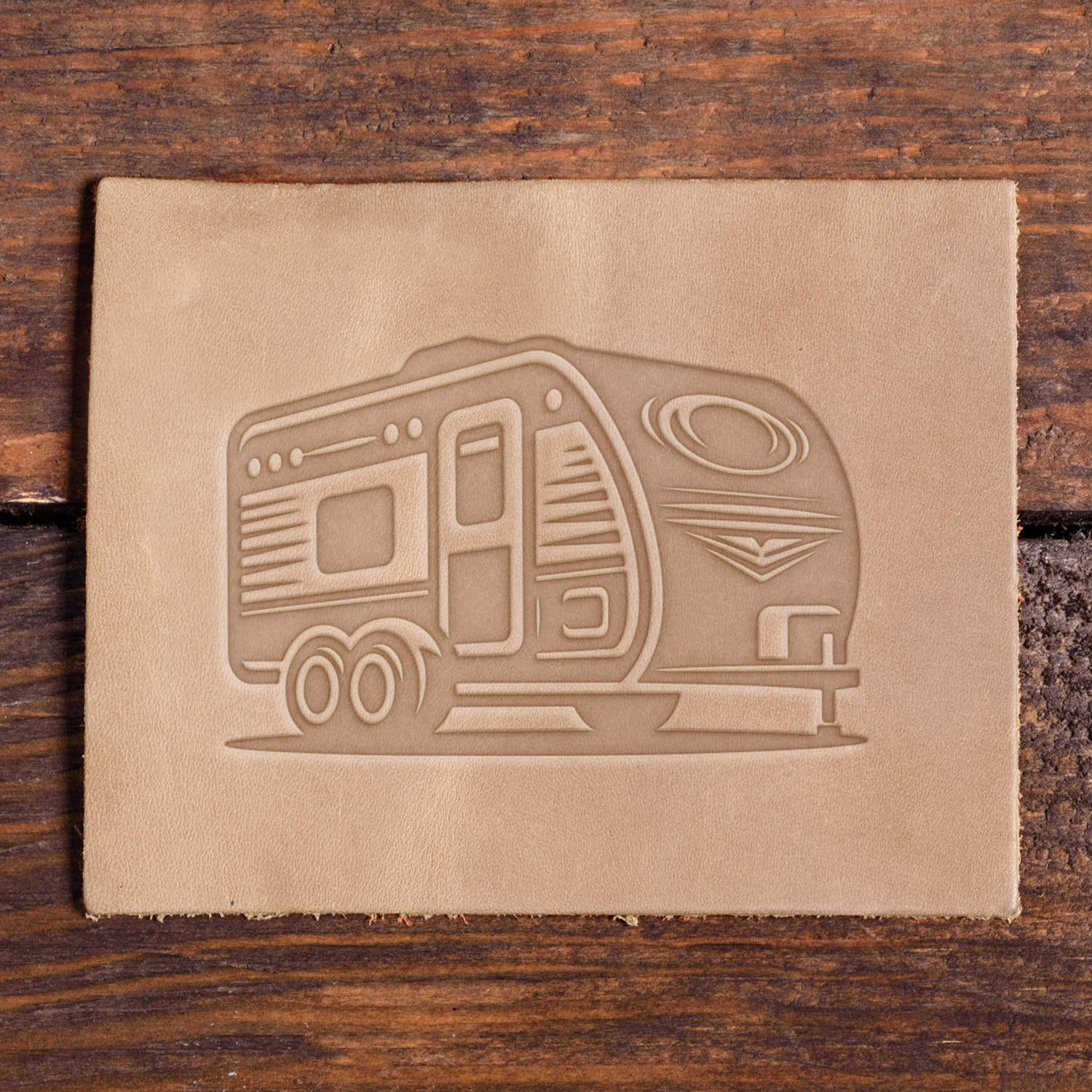 Leather piece stamped with a Delrin leather stamp design of a retro-style camper trailer featuring curved lines and twin wheels.