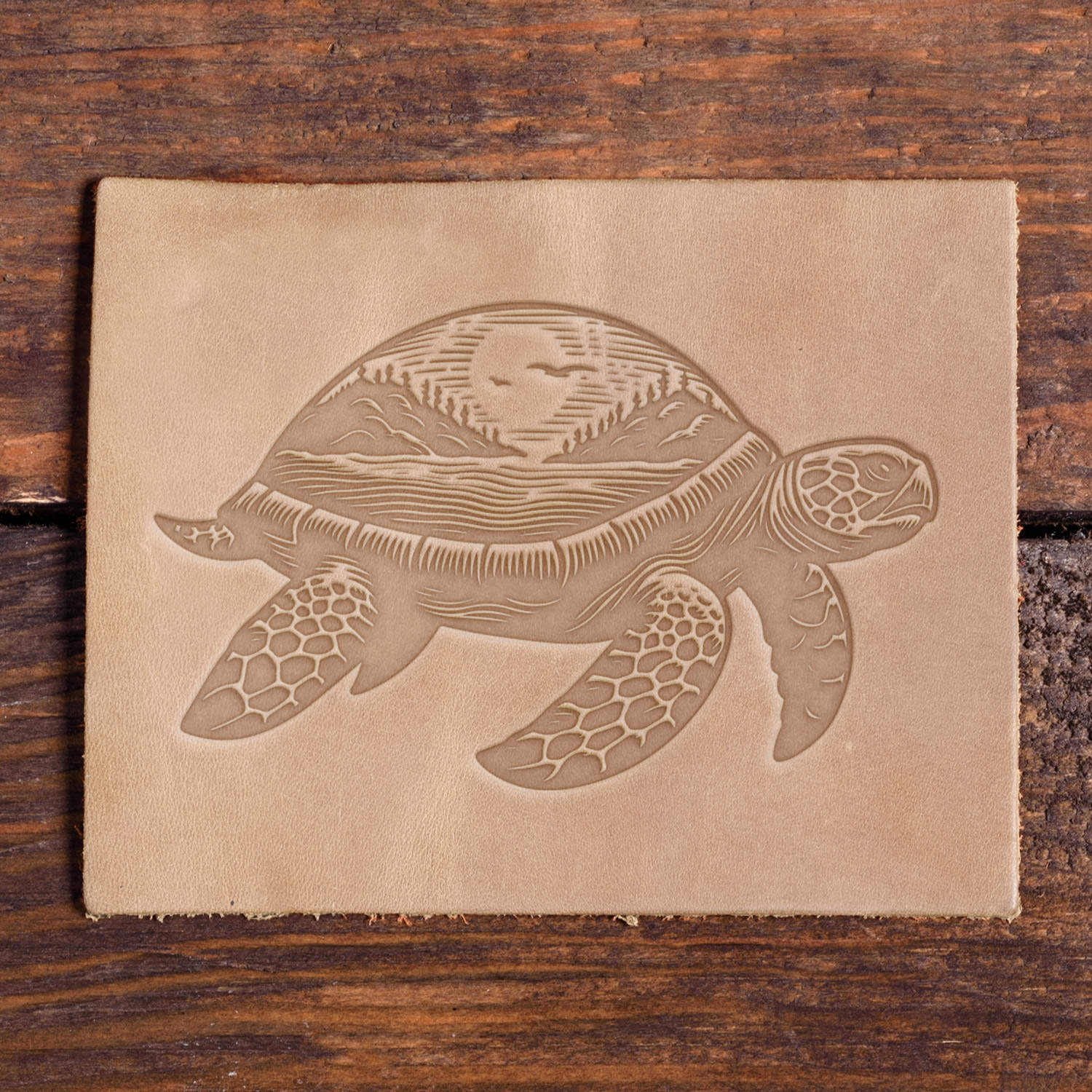 Leather piece stamped with a Delrin leather stamp design of a turtle carrying a scenic landscape on its shell, including waves, trees, and a sunrise.