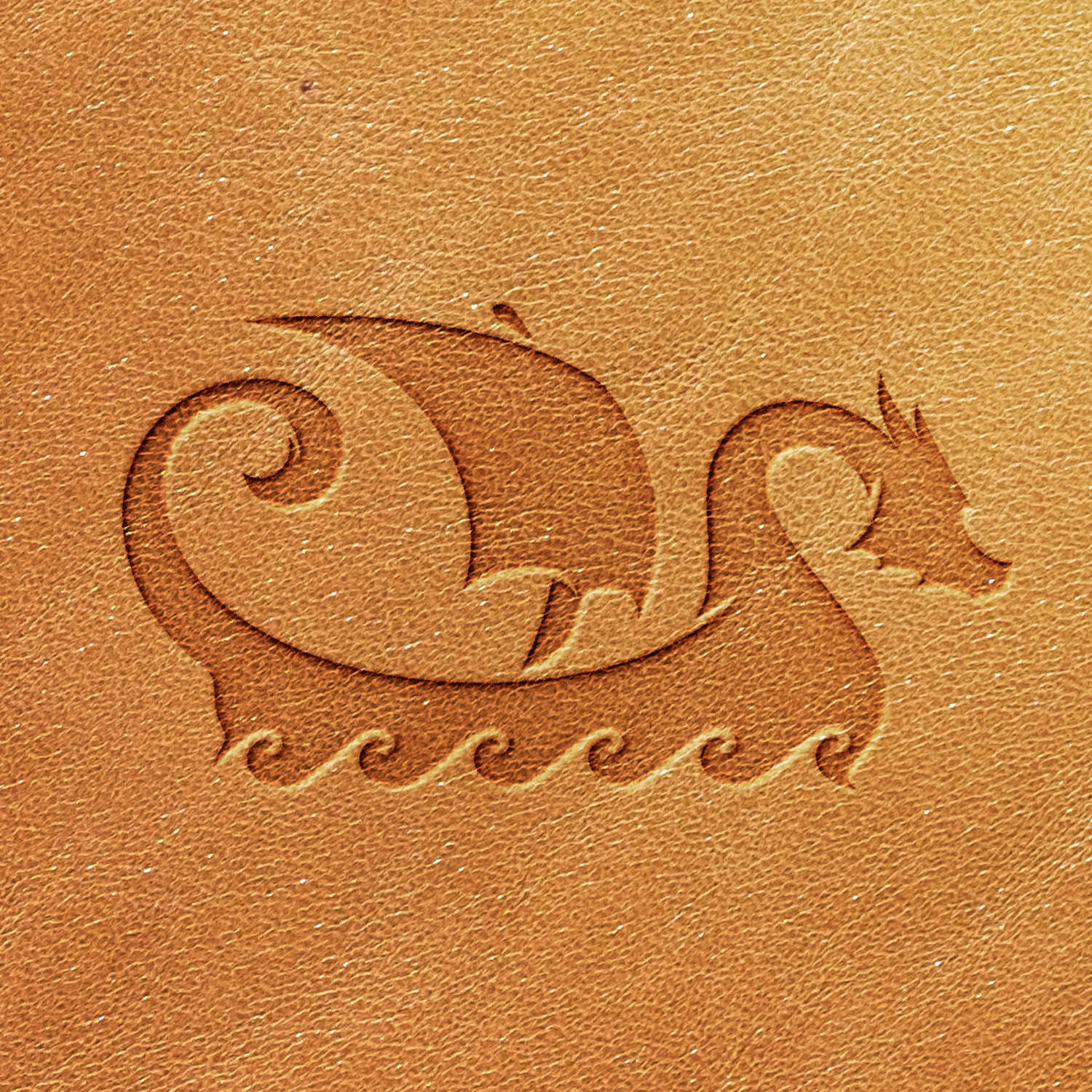 The Viking Ship Delrin Leather Stamp creates a striking leather surface embossed with an illustration of a dragon boat featuring a curled tail and a raised sail, set against wavy water patterns. The embossed design stands out prominently against the leather's texture.