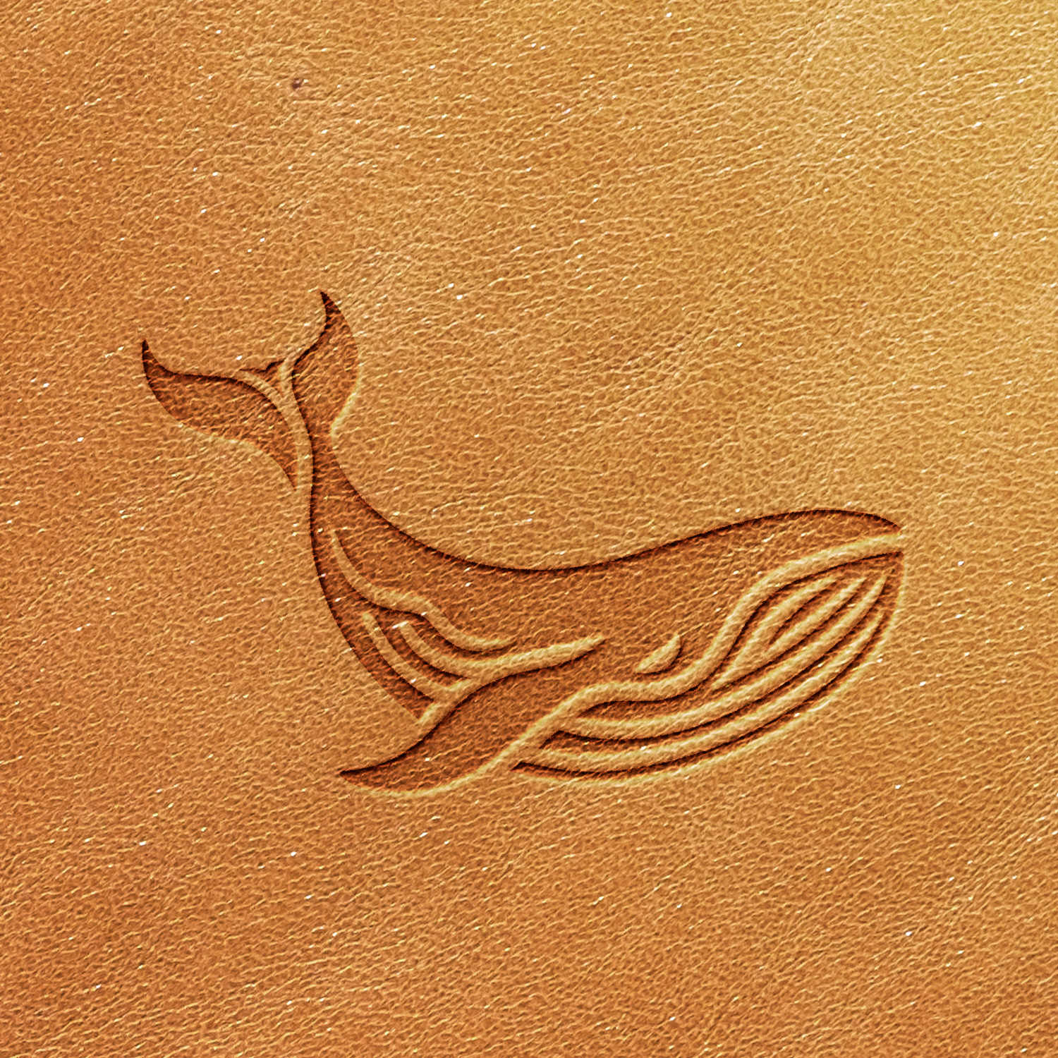 A piece of tan-colored leather with visible texture features an embossed stylized whale design created using the Whale Delrin Leather Stamp, depicted in a simplistic, linear format.