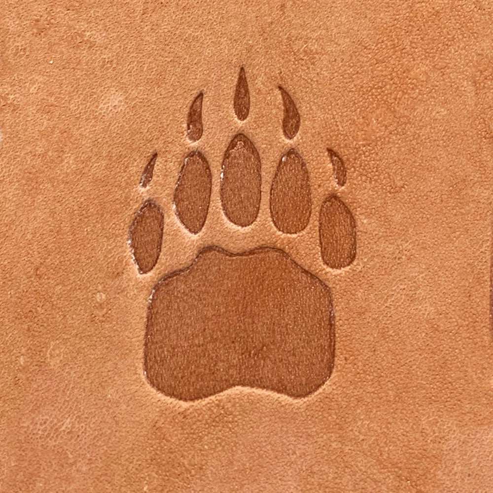 Natural veg-tan leather stamped with a bear paw print using a Delrin leather stamp, showing bold pad shape and defined claw impressions.