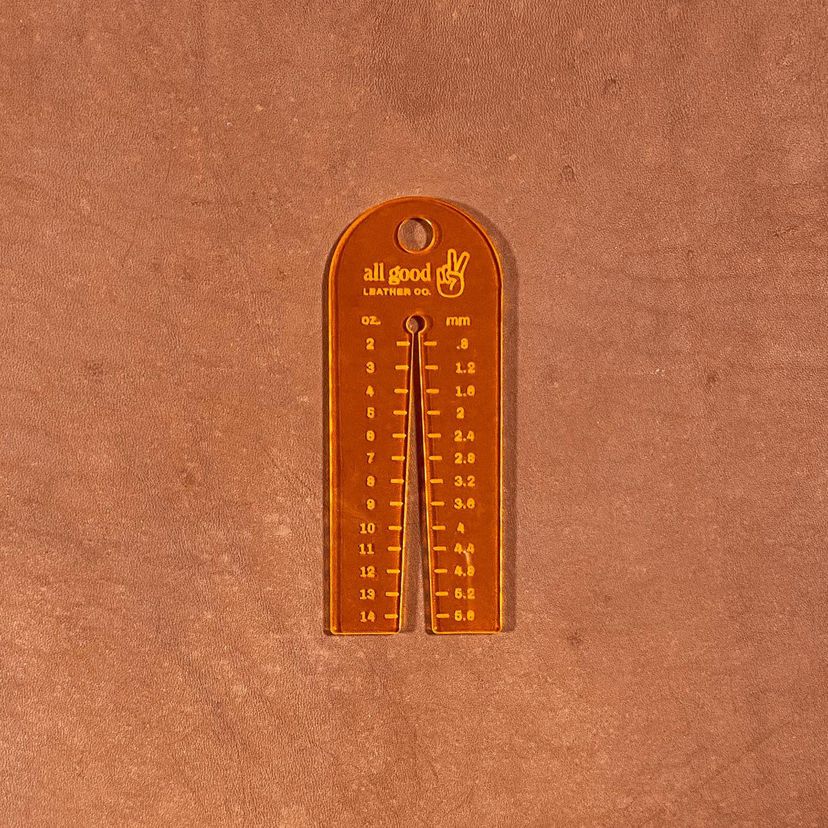Fluorescent orange leather thickness gauge tool resting on vegetable-tanned leather