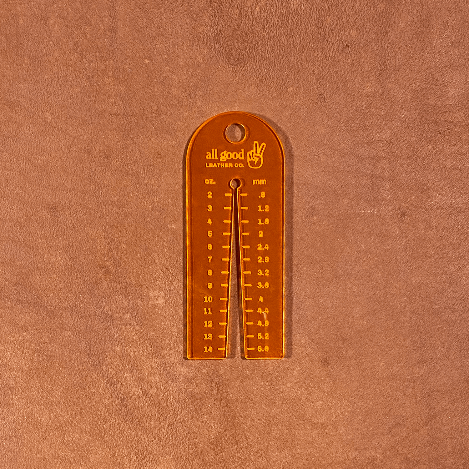Fluorescent orange leather thickness gauge tool resting on vegetable-tanned leather