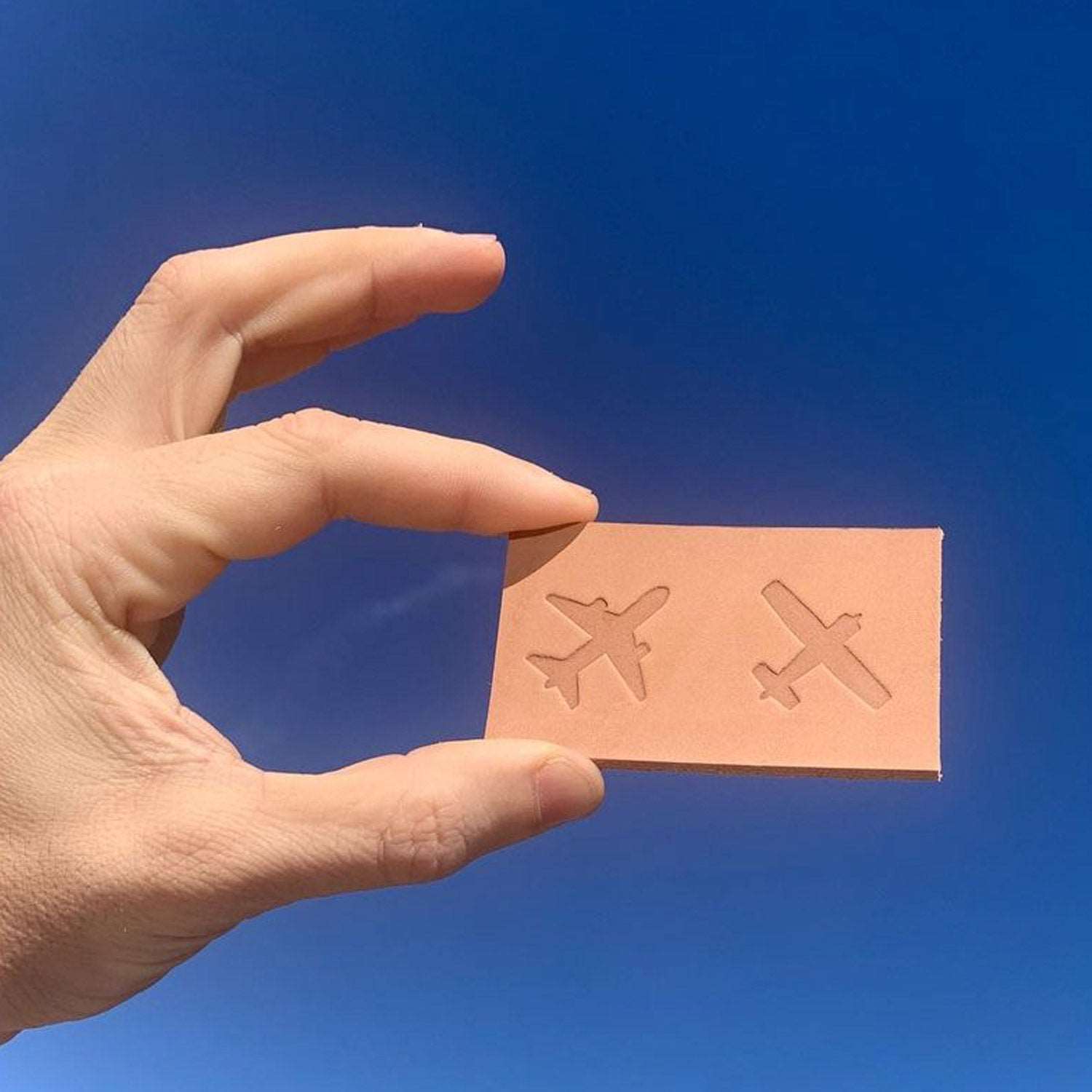 Delrin leather stamp with airplane silhouette stamped into vegetable-tanned leather, held in hand for scale.